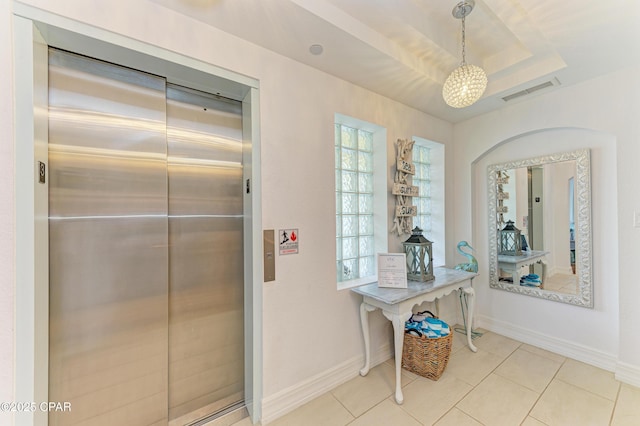 hallway featuring light tile patterned flooring, visible vents, baseboards, a tray ceiling, and elevator