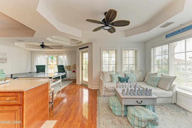 living area featuring a wealth of natural light, a tray ceiling, light wood-style flooring, and baseboards