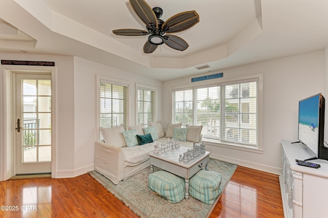 living room with visible vents, baseboards, a ceiling fan, a tray ceiling, and light wood-type flooring