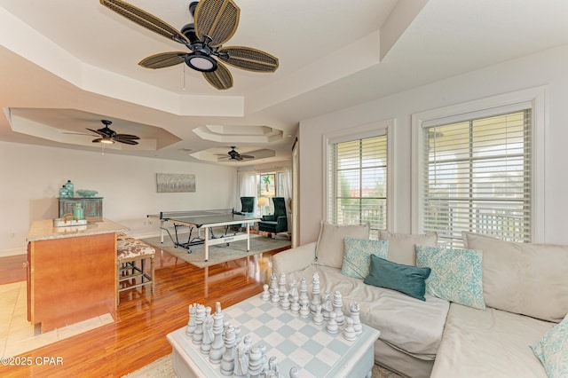 living area with light wood-type flooring, baseboards, and a tray ceiling