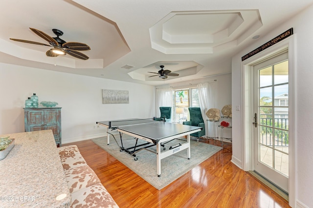 recreation room with light wood-style floors, a tray ceiling, visible vents, and baseboards