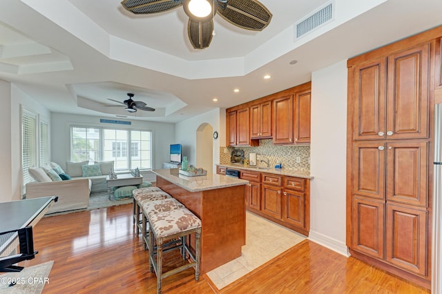 kitchen with a tray ceiling, arched walkways, visible vents, brown cabinetry, and ceiling fan