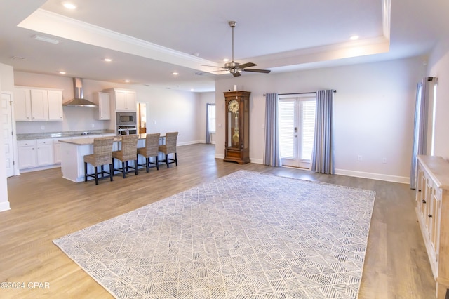 living room with a raised ceiling, light hardwood / wood-style flooring, and ceiling fan