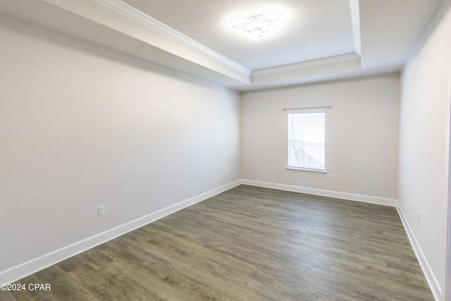 unfurnished room with a raised ceiling, dark wood-type flooring, and crown molding