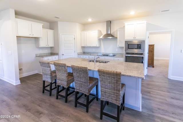 kitchen with a kitchen island with sink, sink, wall chimney exhaust hood, appliances with stainless steel finishes, and white cabinetry