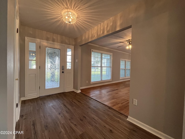 entryway featuring ornamental molding, ceiling fan with notable chandelier, and dark wood-type flooring