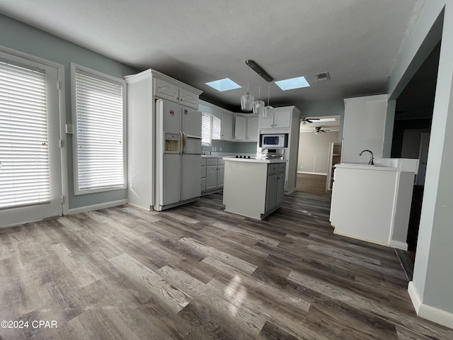 kitchen with a skylight, pendant lighting, white fridge with ice dispenser, dark hardwood / wood-style floors, and stainless steel microwave