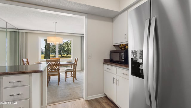 kitchen with light wood-type flooring, a textured ceiling, decorative light fixtures, white cabinets, and stainless steel fridge with ice dispenser