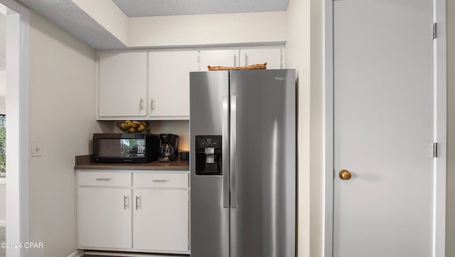 kitchen featuring stainless steel fridge, a textured ceiling, and white cabinetry