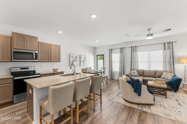 kitchen featuring a kitchen breakfast bar, light stone counters, stainless steel appliances, sink, and light hardwood / wood-style flooring