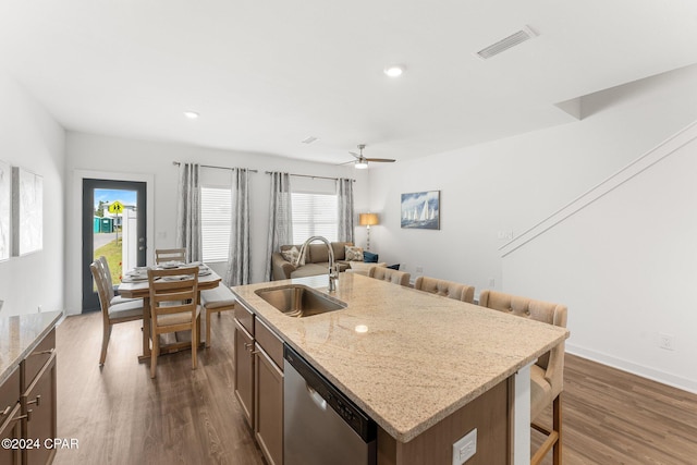 kitchen with light stone countertops, stainless steel dishwasher, sink, a center island with sink, and dark hardwood / wood-style floors