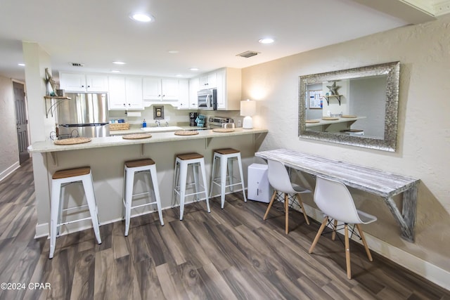 kitchen featuring a breakfast bar, dark hardwood / wood-style floors, white cabinetry, kitchen peninsula, and stainless steel appliances