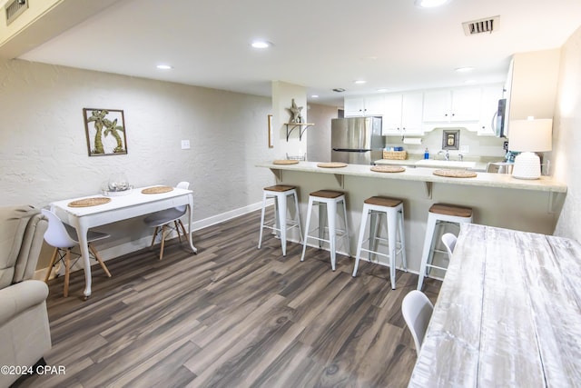 kitchen featuring a breakfast bar, white cabinets, dark hardwood / wood-style floors, kitchen peninsula, and stainless steel appliances