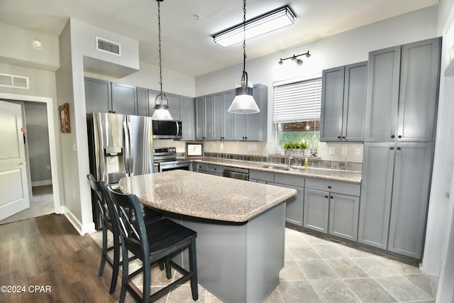 kitchen featuring a center island, sink, decorative light fixtures, light stone counters, and stainless steel appliances