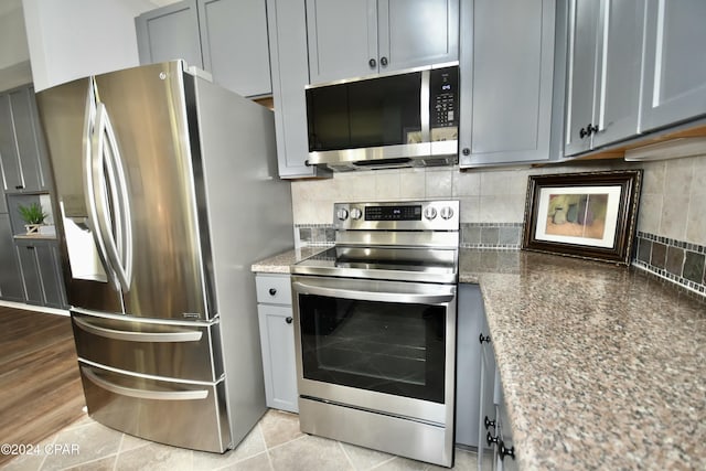 kitchen with dark stone counters, gray cabinetry, stainless steel appliances, and light wood-type flooring