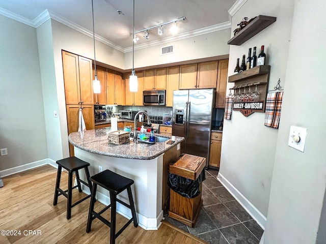 kitchen featuring sink, dark stone countertops, stainless steel appliances, an island with sink, and decorative light fixtures