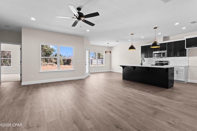 kitchen featuring a kitchen island with sink, hanging light fixtures, wood-type flooring, and appliances with stainless steel finishes