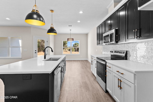 kitchen with pendant lighting, sink, stainless steel appliances, a center island with sink, and decorative backsplash