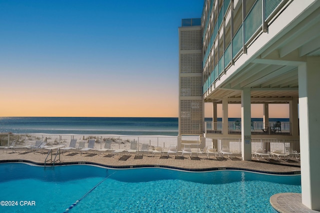 pool at dusk with a patio area and a water view