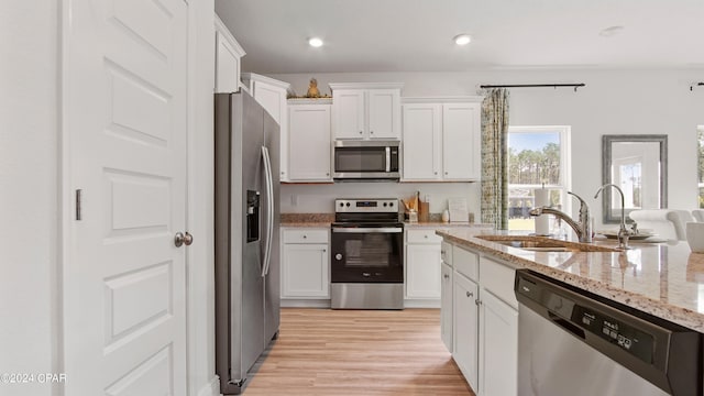 kitchen with appliances with stainless steel finishes, light wood-type flooring, light stone counters, sink, and white cabinets