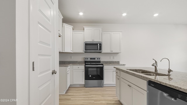 kitchen featuring white cabinets, appliances with stainless steel finishes, light stone countertops, and sink