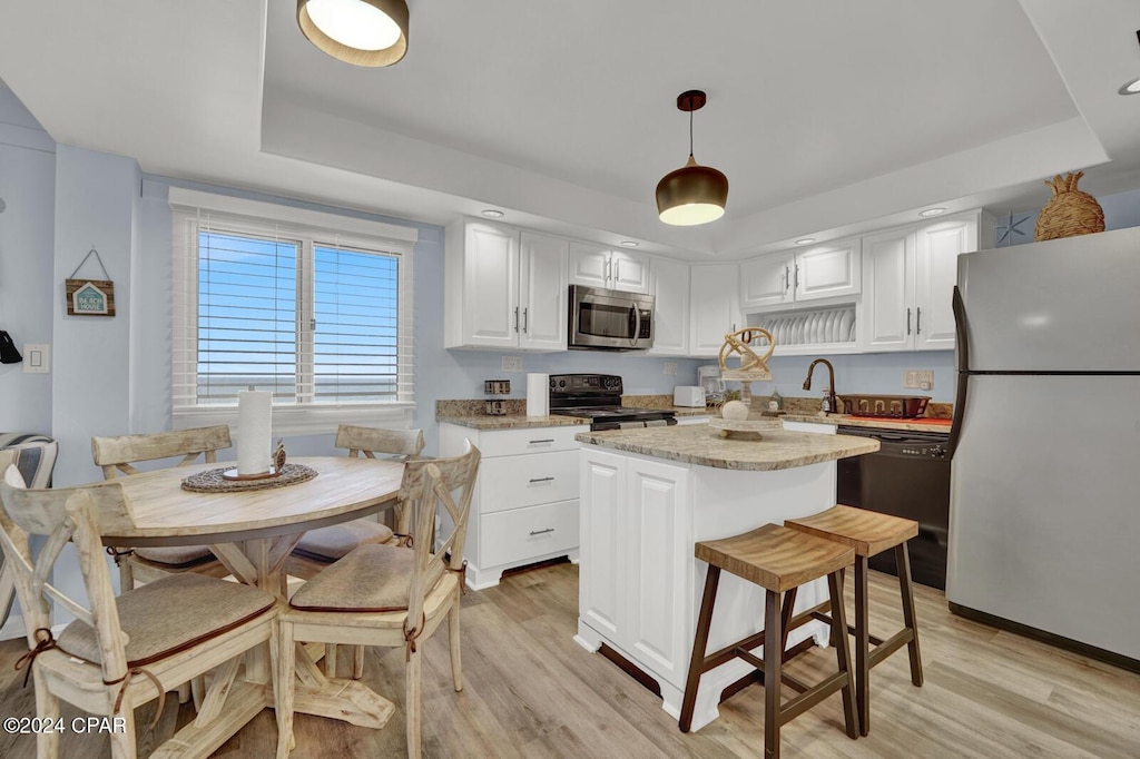 kitchen with hanging light fixtures, white cabinets, light hardwood / wood-style flooring, a kitchen island, and black appliances