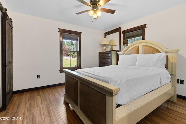 bedroom with dark hardwood / wood-style flooring, ceiling fan, and a barn door