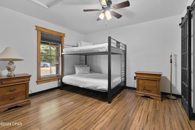 bedroom with a barn door, ceiling fan, and wood-type flooring