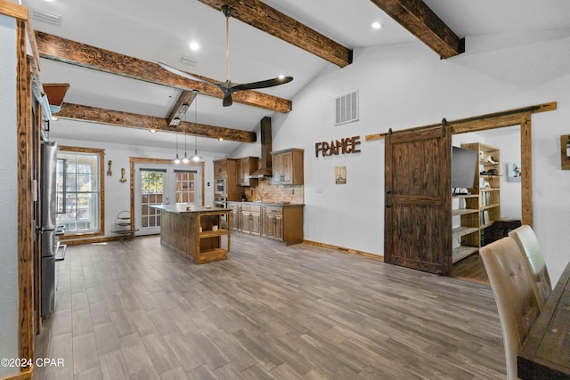 kitchen featuring a barn door, a kitchen island, wood-type flooring, and wall chimney range hood