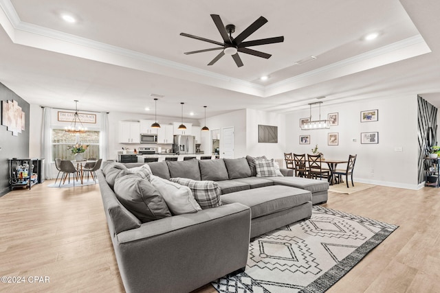 living room with a raised ceiling, ceiling fan with notable chandelier, and light wood-type flooring