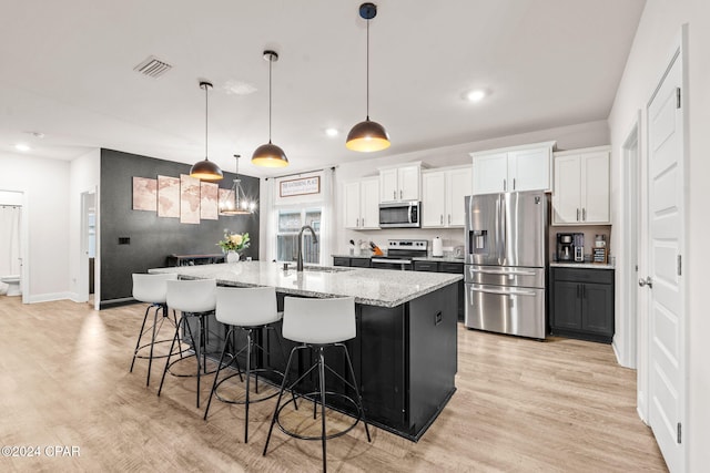 kitchen featuring pendant lighting, white cabinets, a center island with sink, light stone counters, and stainless steel appliances