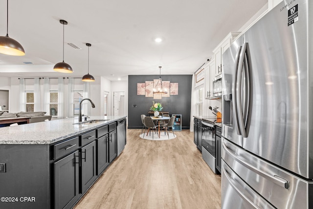 kitchen featuring appliances with stainless steel finishes, sink, hanging light fixtures, and an island with sink