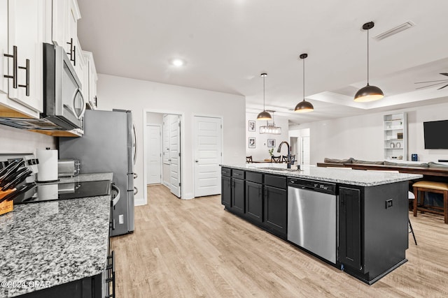 kitchen with stainless steel appliances, a kitchen island with sink, sink, white cabinets, and hanging light fixtures