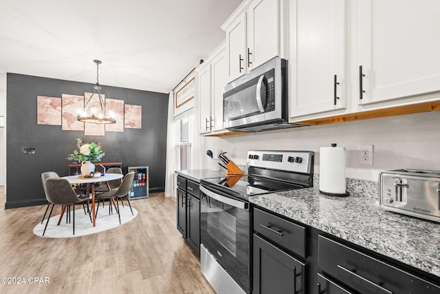 kitchen featuring white cabinetry, stainless steel appliances, light stone counters, a notable chandelier, and light wood-type flooring