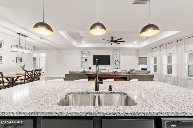 kitchen featuring light stone countertops, ornamental molding, a raised ceiling, sink, and a center island with sink