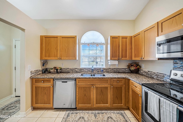 kitchen with dark stone countertops, sink, light tile patterned floors, and stainless steel appliances