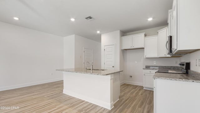 kitchen with white cabinets, light wood-type flooring, a center island with sink, and black range