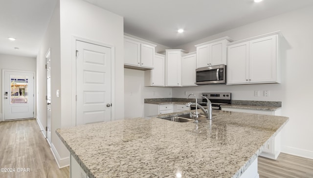 kitchen with white cabinets, appliances with stainless steel finishes, light hardwood / wood-style floors, and a kitchen island with sink