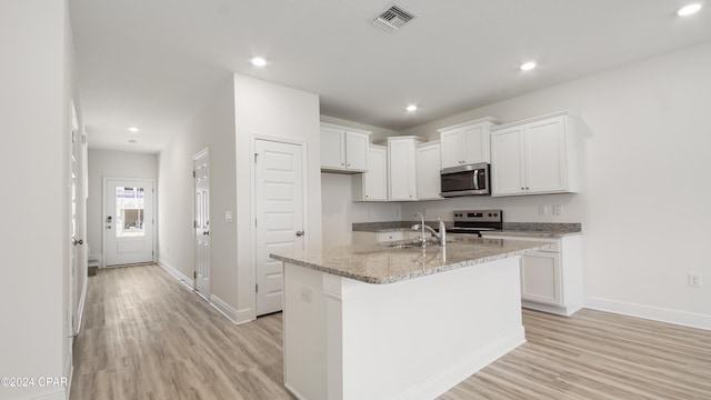 kitchen with light stone countertops, stainless steel appliances, a kitchen island with sink, white cabinets, and light hardwood / wood-style floors