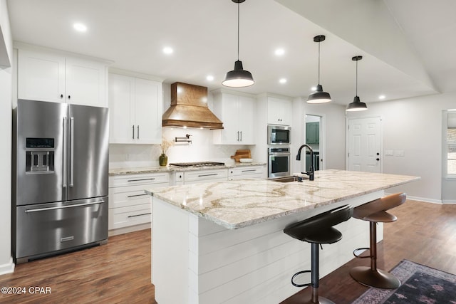 kitchen featuring an island with sink, white cabinets, stainless steel appliances, and custom range hood