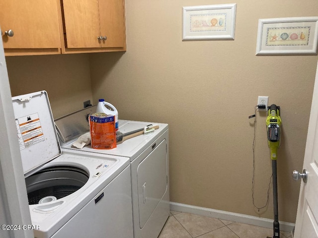 laundry area featuring washing machine and clothes dryer, light tile patterned floors, and cabinets