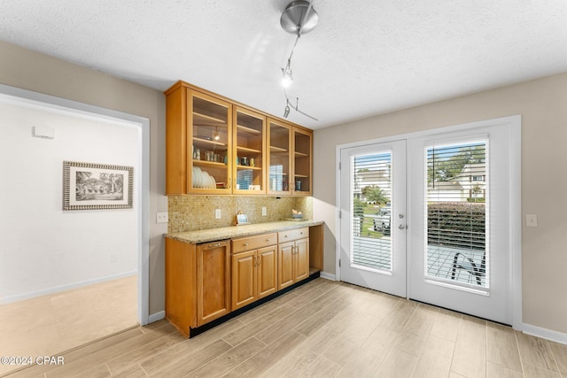 kitchen featuring decorative backsplash, french doors, light wood-type flooring, light stone counters, and a textured ceiling