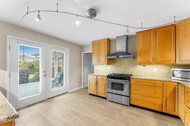 kitchen featuring appliances with stainless steel finishes, rail lighting, french doors, wall chimney range hood, and light hardwood / wood-style floors