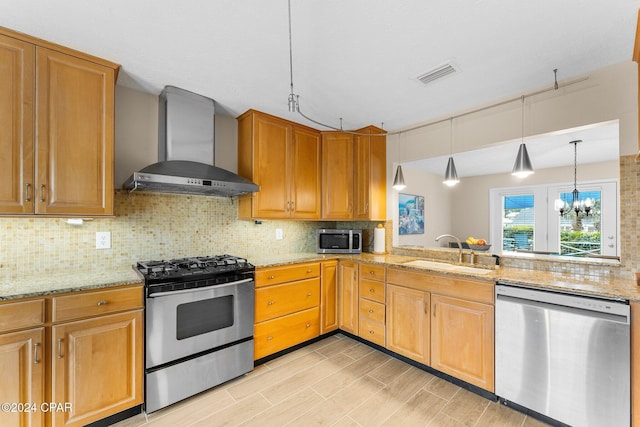 kitchen with appliances with stainless steel finishes, sink, wall chimney range hood, decorative light fixtures, and a notable chandelier