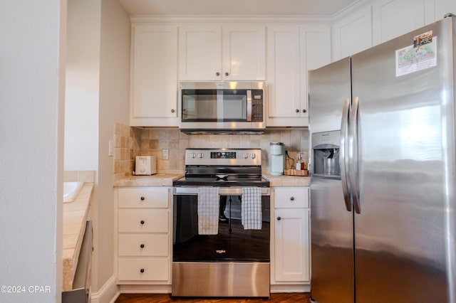 kitchen with backsplash, white cabinets, wood-type flooring, and appliances with stainless steel finishes