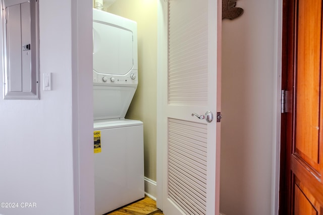 laundry area featuring light wood-type flooring, electric panel, and stacked washer / dryer