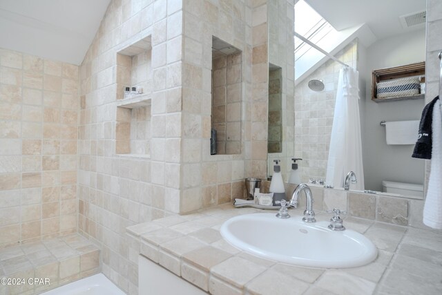 bathroom with toilet, curtained shower, lofted ceiling, and sink