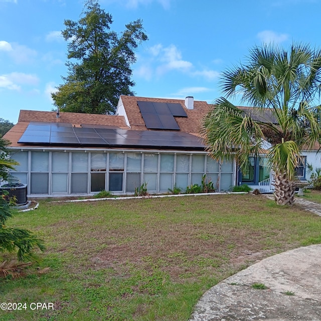 back of property with solar panels, a yard, and central AC unit