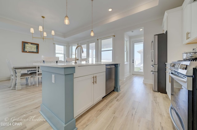 kitchen featuring white cabinets, appliances with stainless steel finishes, decorative light fixtures, and a kitchen island with sink