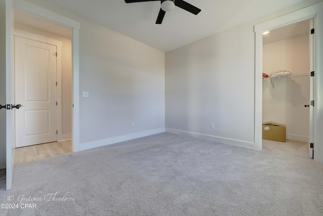 unfurnished bedroom featuring ceiling fan, a walk in closet, light carpet, and a closet